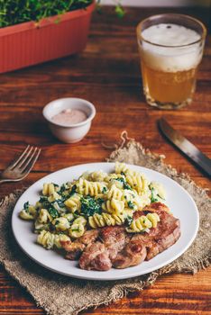 Pork Neck Steak with Creamy Spinach Pasta Garnished with Grated Parmesan Cheese on White Plate