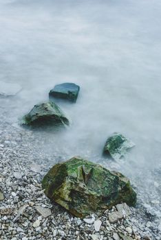 Row of boulders in foam of waves on river coast