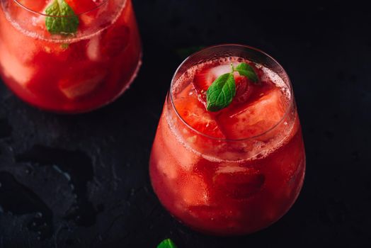 Glasses of cool watermelon and strawberry cocktail with mint garnish on dark concrete background
