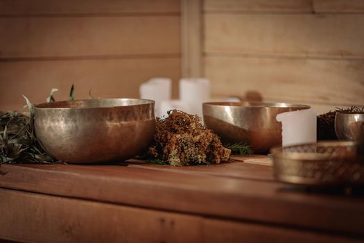 Tibetan singing bowls with bunches of dry grass and candles on a wooden background.