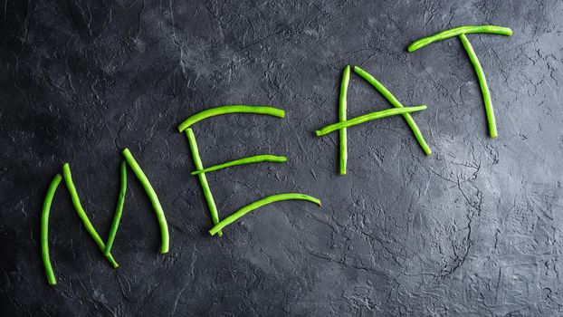Word Meat Spelled Out In Fresh Pods of Green Beans on Dark Concrete Background