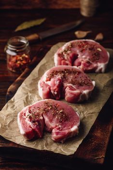 Raw pork loin steaks with different spices on baking paper