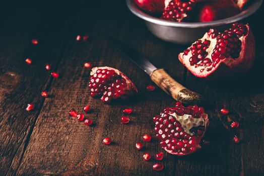 Pomegranate pieces with knife on rustic wooden surface.