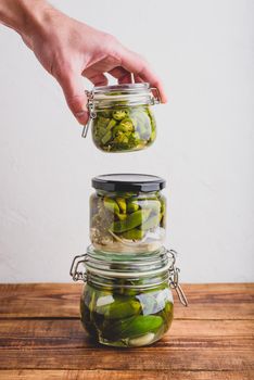 Male Hand Holding One of Three Glass Jars of Freshly Pickled Jalapeno Peppers with Herbs and Garlic. Copy Space