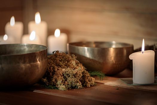 Tibetan singing bowls with bunches of dry grass and candles on a wooden background.