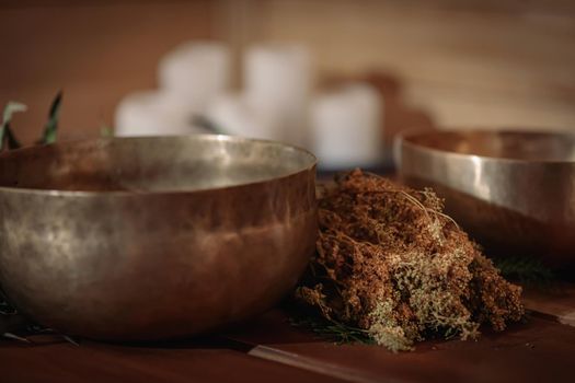 Tibetan singing bowls with bunches of dry grass and candles on a wooden background.