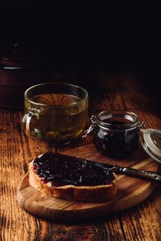 Toast with berry jam on cutting board and cup of green tea in rustic setting