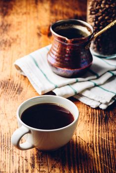 Cup of black coffee with copper cezve and jar of roasted coffee beans on wooden table