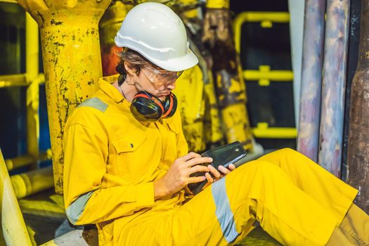 Young man in a yellow work uniform, glasses and helmet in industrial environment,oil Platform or liquefied gas plant. looking into his empty wallet. Do not pay salary.