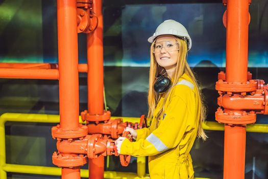 Young woman in a yellow work uniform, glasses and helmet in industrial environment,oil Platform or liquefied gas plant.