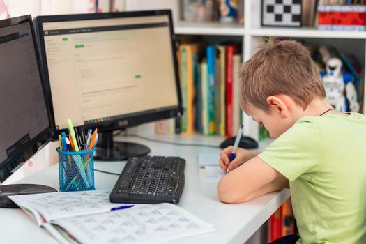 Little young school boy working at home with a laptop and class notes studying in a virtual class. Distance education and learning, e-learning, online learning concept during quarantine