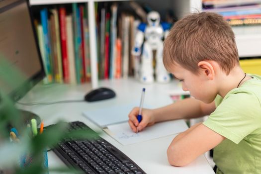 Little young school boy working at home with a laptop and class notes studying in a virtual class. Distance education and learning, e-learning, online learning concept during quarantine