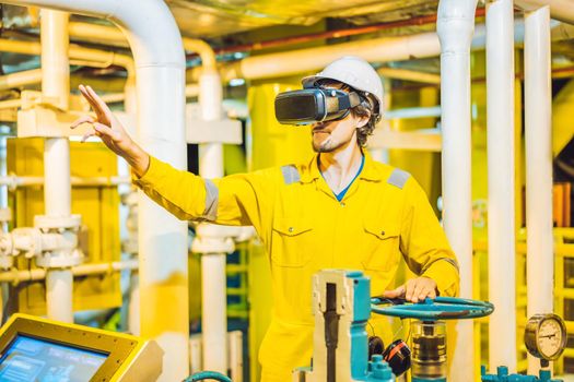 Young woman in a yellow work uniform, glasses and helmet uses virtual reality glasses in industrial environment,oil Platform or liquefied gas plant.