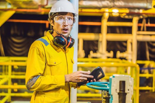 Young man in a yellow work uniform, glasses and helmet in industrial environment,oil Platform or liquefied gas plant. looking into his empty wallet. Do not pay salary.