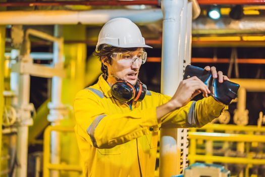 Young man in a yellow work uniform, glasses and helmet in industrial environment,oil Platform or liquefied gas plant. looking into his empty wallet. Do not pay salary.