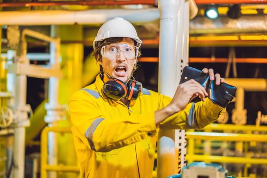 Young man in a yellow work uniform, glasses and helmet in industrial environment,oil Platform or liquefied gas plant. looking into his empty wallet. Do not pay salary.