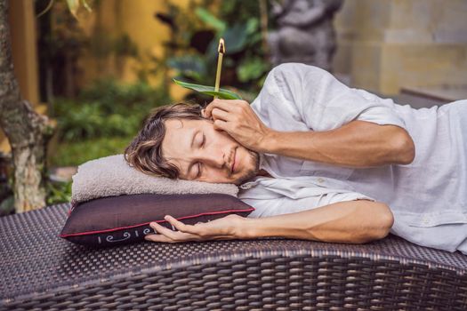 man having an ear candle therapy against the backdrop of a tropical garden.