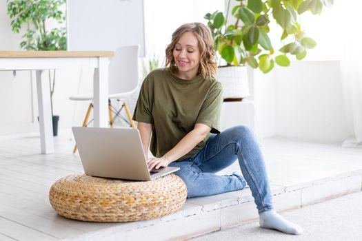 Woman using laptop computer while sitting floor at home interior. Freelance female working from home Distance learning student relaxing and watch lessons on video conference .