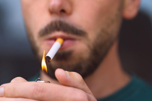 Closeup of young man lighting cigarette with lighter. Smoking cigarette and nicotine addiction. High quality photo