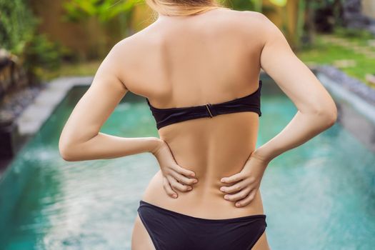 Women's back hurts against the backdrop of the pool. Pool helps with back pain.