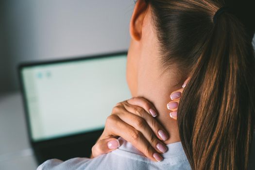 Woman massaging her neck to relieve neck pain after working on laptop. High quality photo
