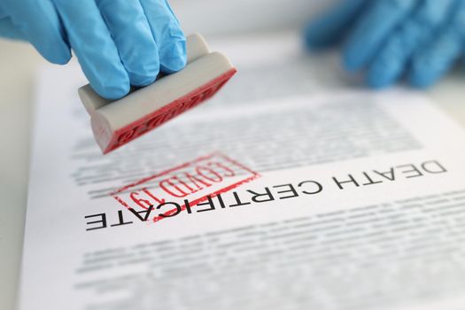 Pathologist putting red covid19 stamp on death certificate closeup. Mortality from coronavirus infection concept