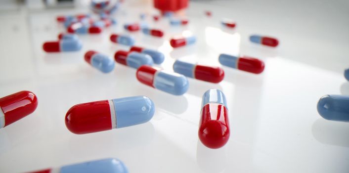 Lot of blue and red capsules lying on white table closeup background. Pharmaceutical industry concept.