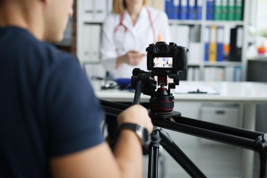 Photographer filming doctor on camera using tripod and slider closeup. Freelance work of photographer and videographer concept