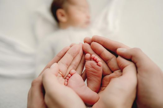 Parents hands holding tiny feet of newborn baby boy closeup while he sleeping. Family portrait with sweet infant child napping