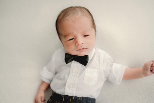 Newborn baby boy wearing festive costume with bow-tie falling asleep. Infant child kid holiday studio portrait