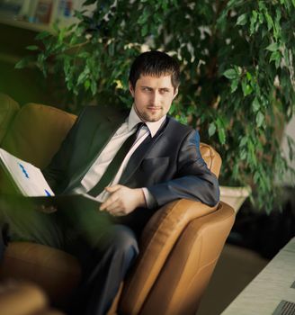 Relaxed businessman sitting at Desk in front of the Windows of the office holding .