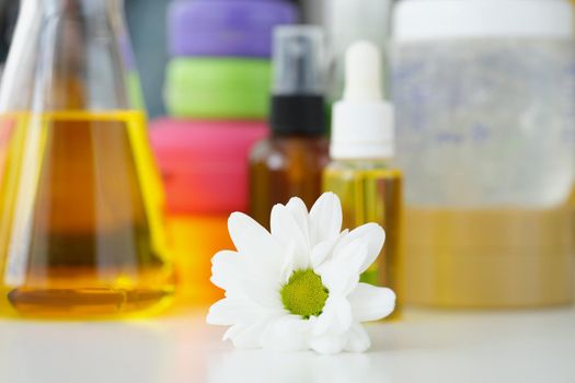 Close-up of chamomile flower and bottles with oils and other cosmetology products on background. Flasks with skincare, wellness. Body and face care concept