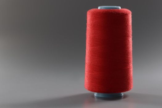 Close-up of red colour thread spool on grey background, yarn for sewing, bright thread for dressmaking. Hobby, tailoring, atelier shop concept. Copy space