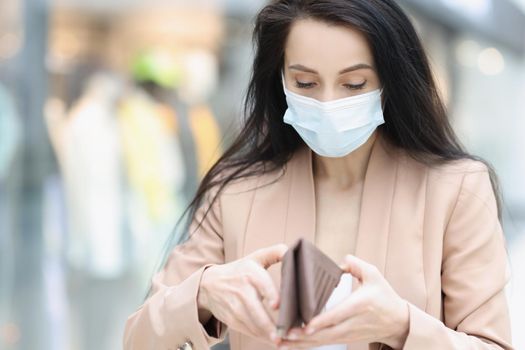 Portrait of woman in face mask look in wallet, female being short of money. Not enough money to pay for purchase, lack of cash. Financial problem concept