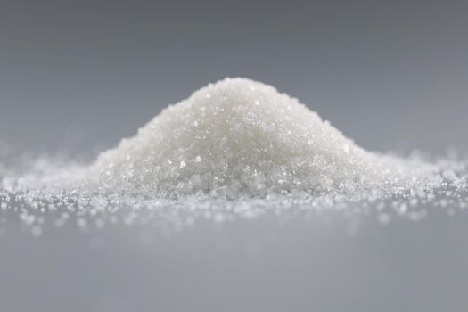 Close-up of sugar crystals pile on grey background, focus on heap of sweet powder, add in dishes or drinks. Ingredient, cooking, sugar substitute concept