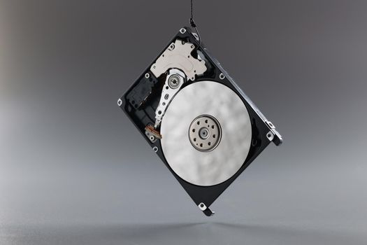 Close-up of computer hard disk drive on hook, black hardware disk, memory storage cylinder on grey background. Technology, digital part, component concept