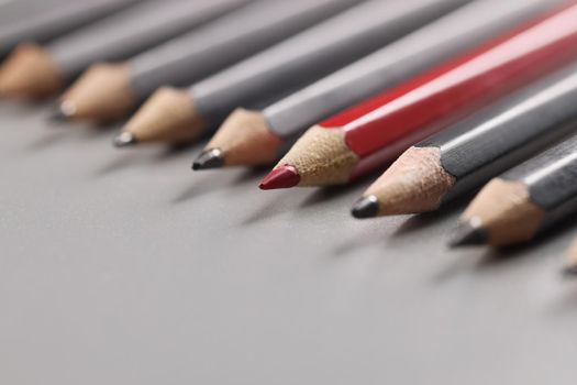 Close-up of pencils tips put on grey surface in strict order, red one among black pens. Idea of creativity and uniqueness. Stay different, leader concept