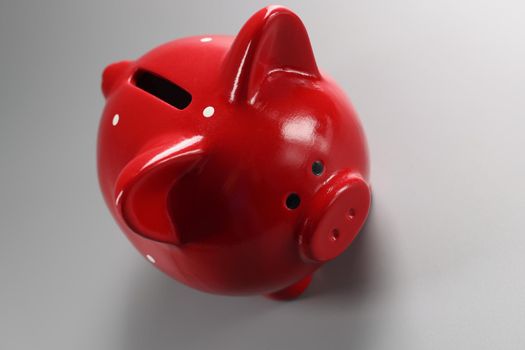 Close-up of red piggybank container on grey surface with hole for coins, empty ceramic pig for money. Finance, saveup for future, success, cash concept