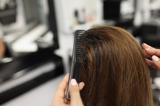 Close-up of professional hairdresser brushing clients hair with comb, shiny hairstyle. Female client sit in masters chair. Wellness, beauty salon concept