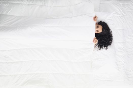 Top view of woman laying on white bedding covering with blanket, wake up well rested in morning, king size bed. Comfort, sleep, rest, chill, hide concept