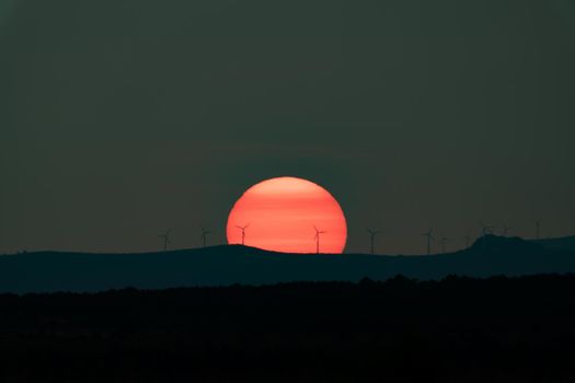 Huge orange sun at sunset with windmills silhouette