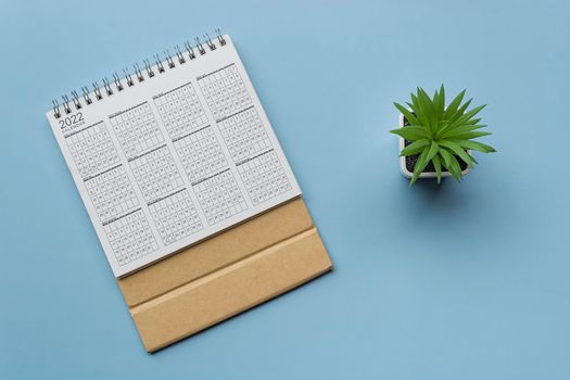 2022 white calendar with potted plant on blue background. Directly above. Flat lay. Resolution and annual plan concept.