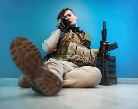 male soldier in camouflage is sitting by an ammunition crate on the floor with a weapon