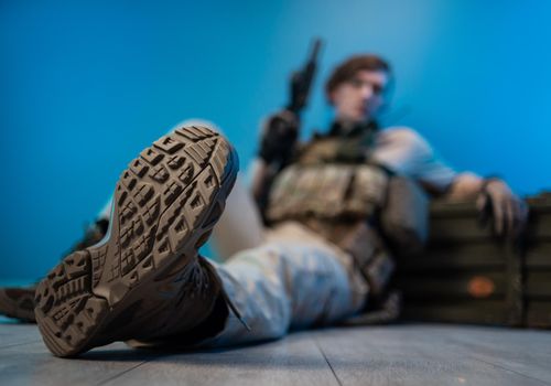 male soldier in camouflage is sitting by an ammunition crate on the floor with a weapon