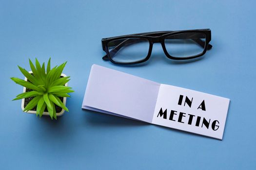 In a meeting text on notepad with reading glasses and potted plant. Directly above. Flat lay, Message and reminder concept.