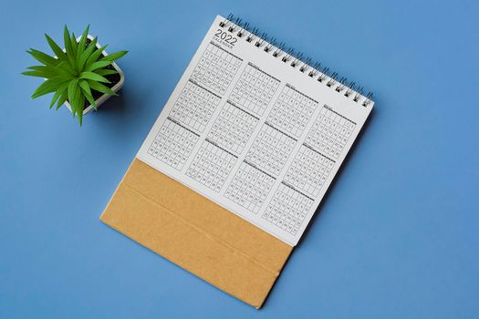 2022 white calendar with potted plant on blue background. Directly above. Flat lay. Resolution and annual plan concept.