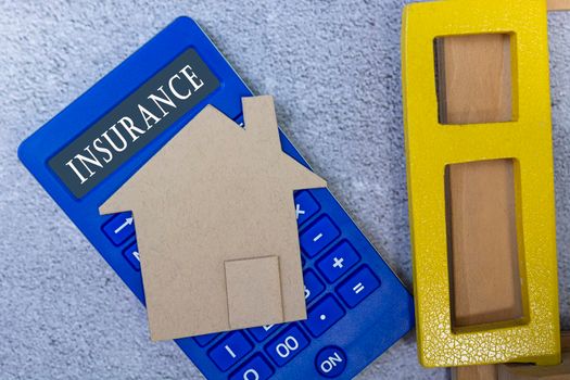 Insurance text on calculator with paper house model and window frame on a desk. Home insurance concept.