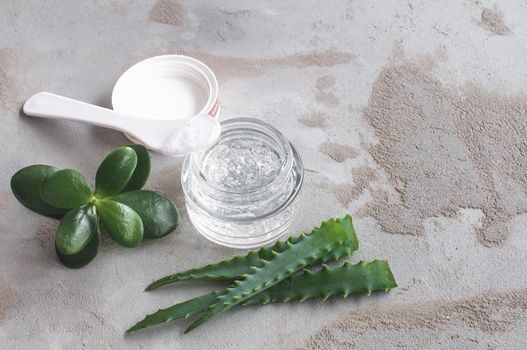 Gel texture with bubbles hyaluronic acid and aloe vera branches in a glass jar on a concrete background