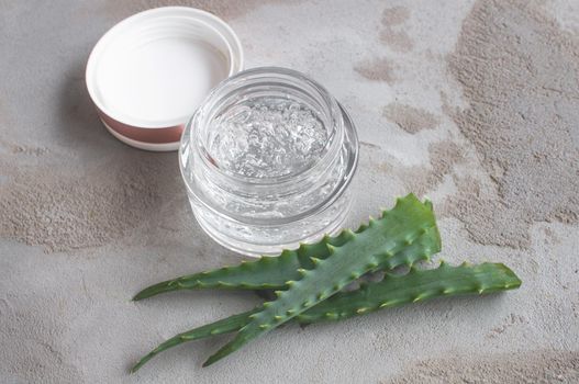 Gel texture with bubbles hyaluronic acid and aloe vera branches in a glass jar on a concrete background