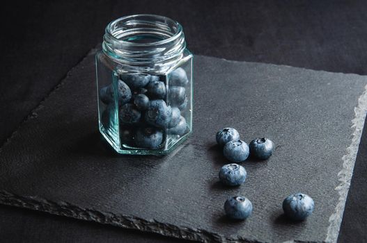 Fresh blueberries in a glass jar and laid out on a black board. Blueberries for a healthy diet and vegetarians